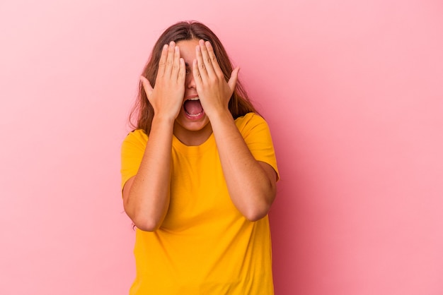 Jeune femme caucasienne isolée sur fond rose s'amusant couvrant la moitié du visage avec la paume.