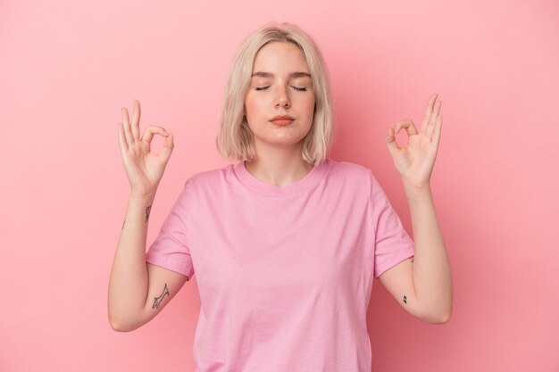 Jeune femme caucasienne isolée sur fond rose se détend après une dure journée de travail, elle fait du yoga.