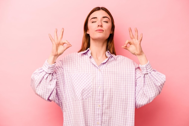 Jeune femme caucasienne isolée sur fond rose se détend après une dure journée de travail, elle fait du yoga