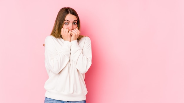 Jeune femme caucasienne isolée sur fond rose se mordant les ongles, nerveuse et très anxieuse.