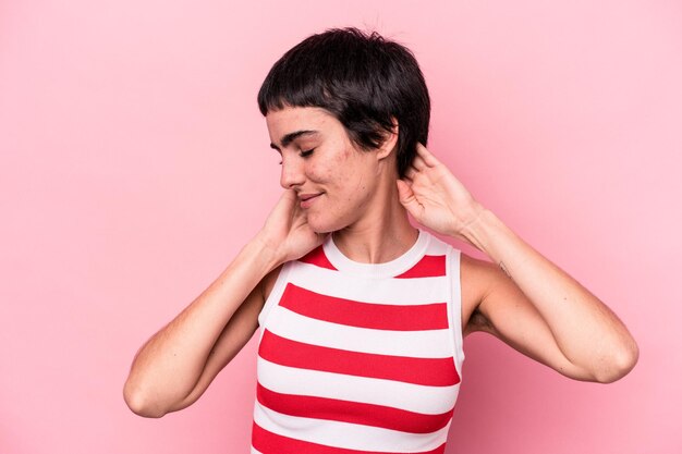 Jeune femme caucasienne isolée sur fond rose se sentant confiante, les mains derrière la tête.