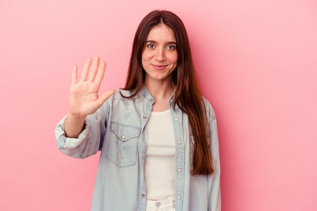 Jeune femme caucasienne isolée sur fond rose souriant gai montrant le numéro cinq avec les doigts.