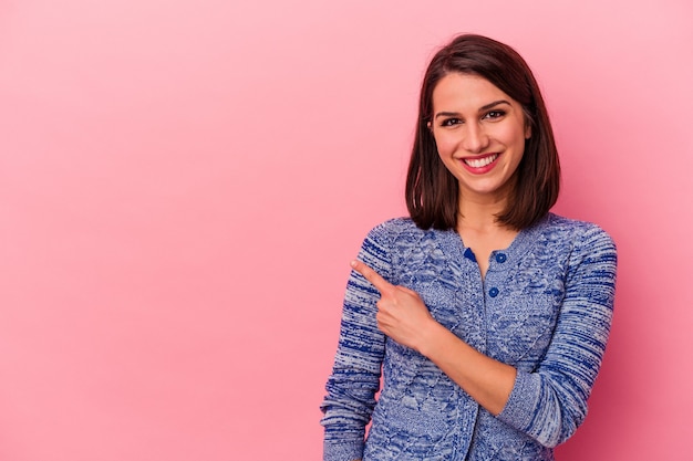 Jeune femme caucasienne isolée sur fond rose souriante et pointant de côté, montrant quelque chose dans un espace vide.