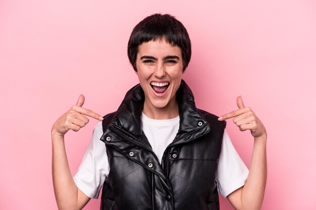 Jeune femme caucasienne isolée sur fond rose surprise pointant du doigt, souriant largement.