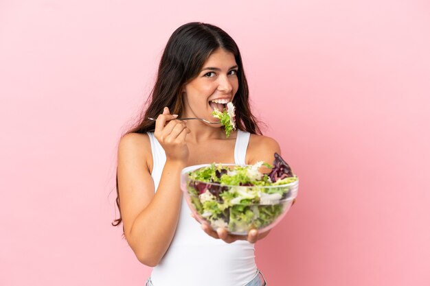 Jeune femme caucasienne isolée sur fond rose tenant un bol de salade avec une expression heureuse