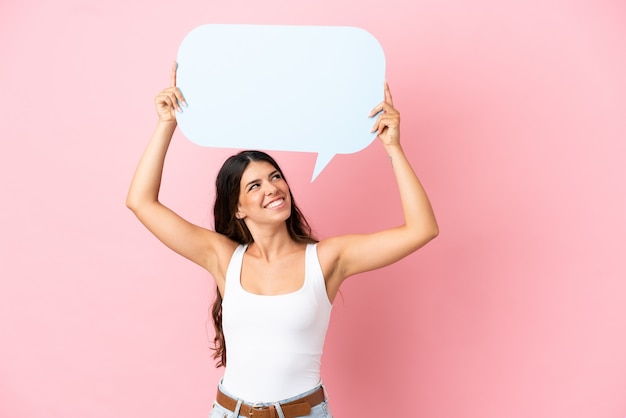 Jeune femme caucasienne isolée sur fond rose tenant une bulle de dialogue vide