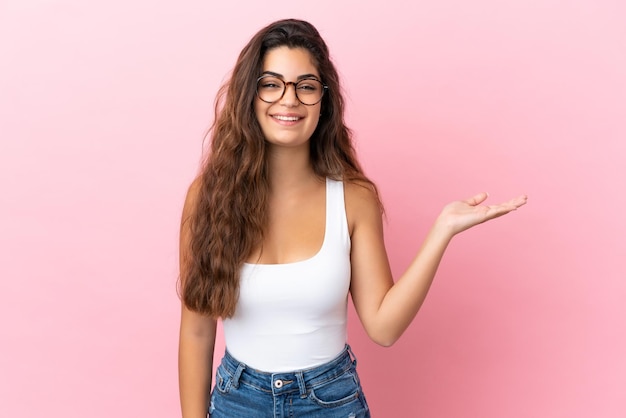 Jeune femme caucasienne isolée sur fond rose tenant un espace de copie imaginaire sur la paume pour insérer une annonce