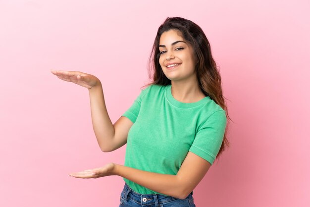 Jeune femme caucasienne isolée sur fond rose tenant un espace de copie pour insérer une annonce