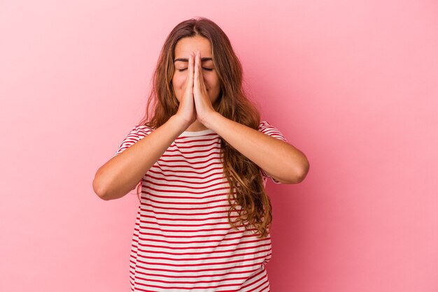 Jeune femme caucasienne isolée sur fond rose tenant la main en prière près de la bouche, se sent confiante.