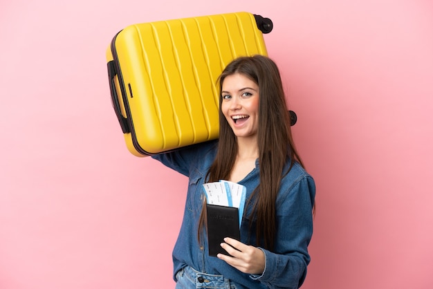 Jeune femme caucasienne isolée sur fond rose en vacances avec valise et passeport