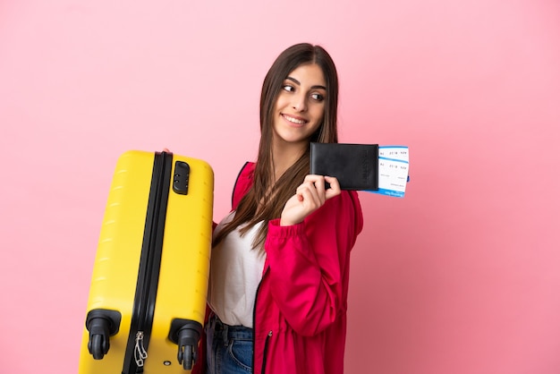 Jeune femme caucasienne isolée sur fond rose en vacances avec valise et passeport