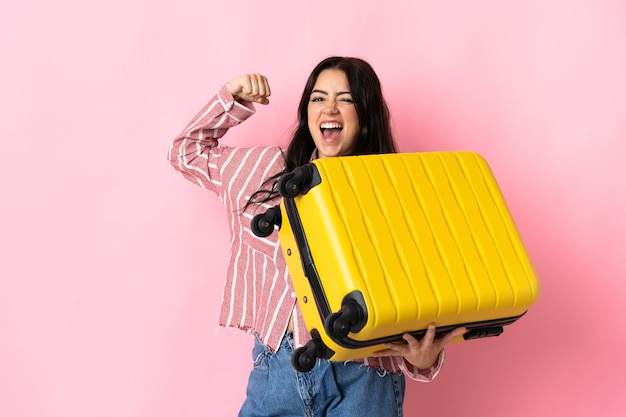 Jeune femme caucasienne isolée sur fond rose en vacances avec valise de voyage