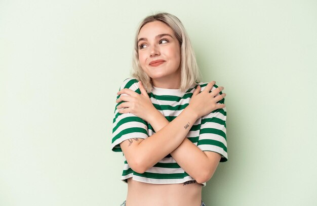 Jeune femme caucasienne isolée sur fond vert câlins, souriante insouciante et heureuse.