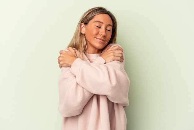 Jeune femme caucasienne isolée sur fond vert câlins, souriante insouciante et heureuse.