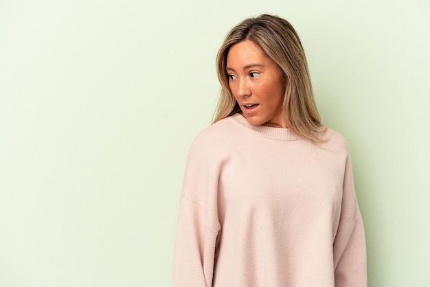 Jeune femme caucasienne isolée sur fond vert choquée à cause de quelque chose qu'elle a vu.