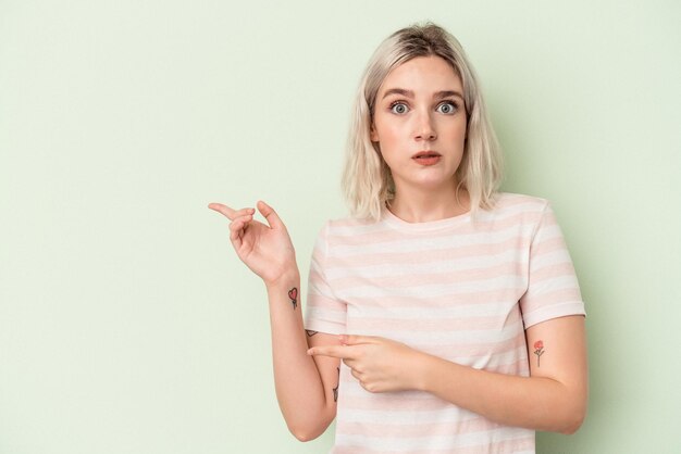 Jeune femme caucasienne isolée sur fond vert choquée pointant avec l'index vers un espace de copie.