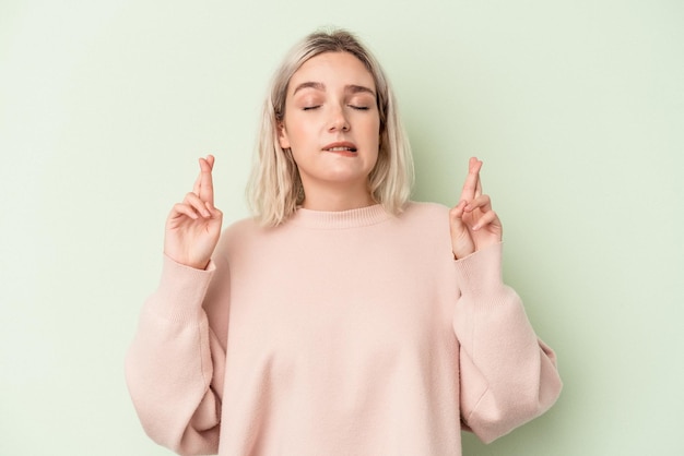 Jeune femme caucasienne isolée sur fond vert croisant les doigts pour avoir de la chance