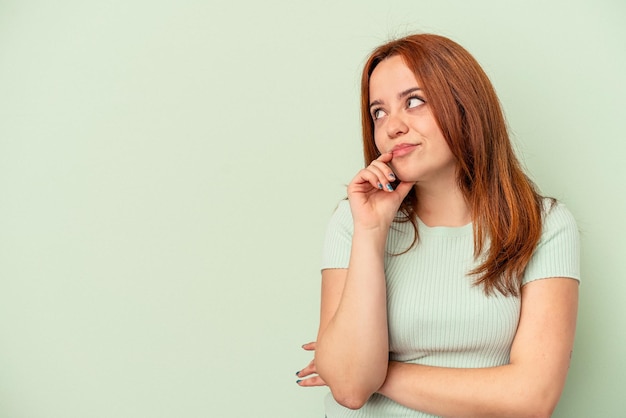 Jeune femme caucasienne isolée sur fond vert détendue en pensant à quelque chose en regardant un espace de copie.