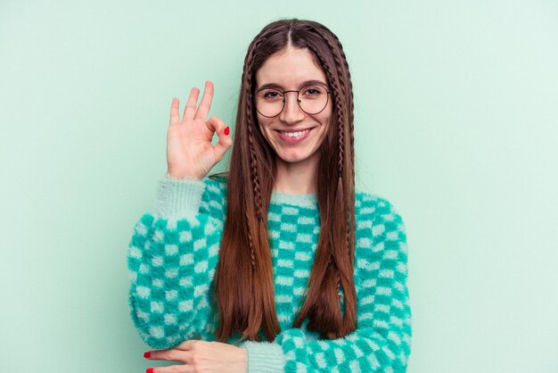 Jeune femme caucasienne isolée sur fond vert fait un clin d'œil et tient un geste correct avec la main.