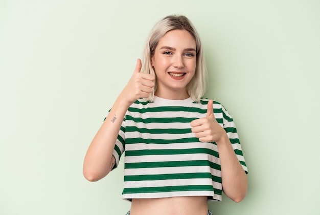 Jeune femme caucasienne isolée sur fond vert levant les deux pouces vers le haut, souriant et confiant.