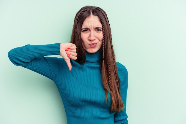 Jeune femme caucasienne isolée sur fond vert montrant le pouce vers le bas, concept de déception.