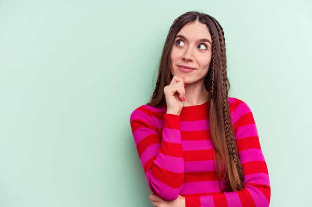 Jeune femme caucasienne isolée sur fond vert regardant de côté avec une expression douteuse et sceptique