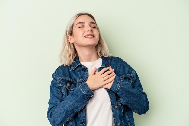 Jeune femme caucasienne isolée sur fond vert en riant en gardant les mains sur le cœur, concept de bonheur.