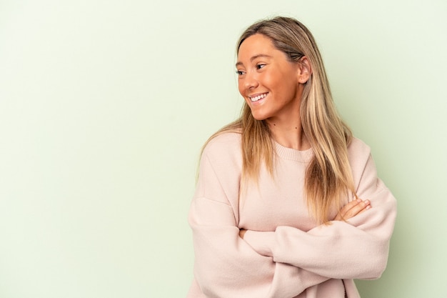 Jeune femme caucasienne isolée sur fond vert souriant confiant avec les bras croisés.