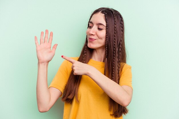 Jeune femme caucasienne isolée sur fond vert souriant joyeux montrant le numéro cinq avec les doigts.