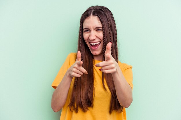 Jeune femme caucasienne isolée sur fond vert sourires joyeux pointant vers l'avant.