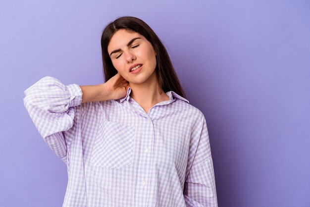 Jeune femme caucasienne isolée sur fond violet ayant une douleur au cou due au stress, en la massant et en la touchant avec la main.