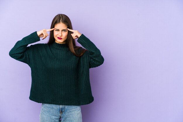 Jeune femme caucasienne isolée sur fond violet concentré sur une tâche, gardant l'index pointant la tête.