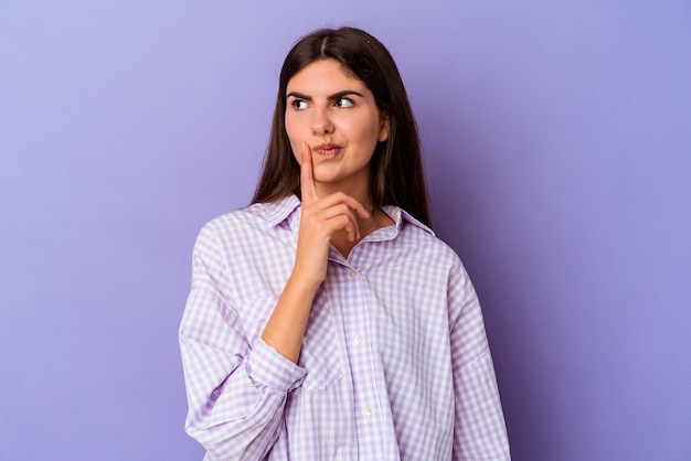 Jeune femme caucasienne isolée sur fond violet contemplant, planifiant une stratégie, réfléchissant à la manière d'une entreprise.