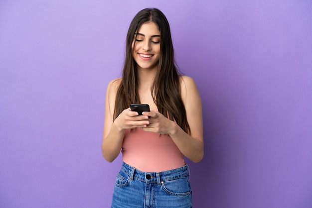 Jeune femme caucasienne isolée sur fond violet envoyant un message avec le mobile