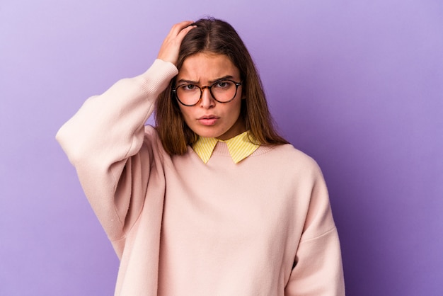 Jeune femme caucasienne isolée sur fond violet fatiguée et très endormie en gardant la main sur la tête.