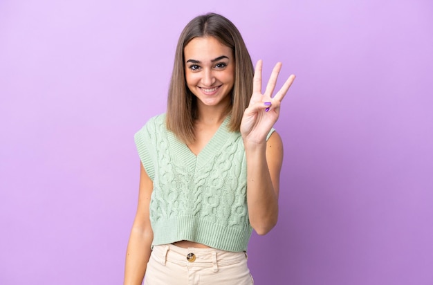 Jeune femme caucasienne isolée sur fond violet heureuse et comptant trois avec les doigts