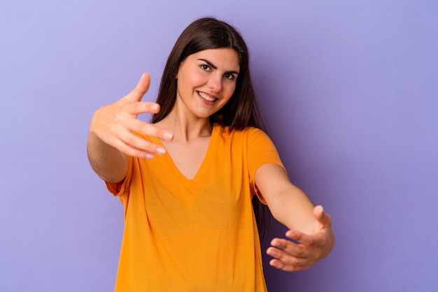 Jeune femme caucasienne isolée sur fond violet montrant une expression de bienvenue.