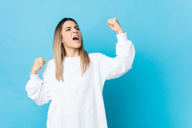 Jeune femme caucasienne isolée levant le poing après une victoire, concept gagnant.