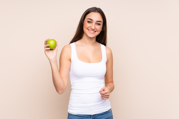 Jeune femme caucasienne isolée sur un mur beige avec une pomme et heureux