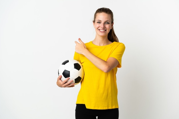 Jeune femme caucasienne isolée sur un mur blanc avec ballon de foot et pointant vers le côté