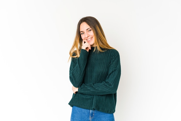 Jeune femme caucasienne isolée sur mur blanc souriant heureux et confiant, toucher le menton avec la main.