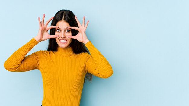 Jeune femme caucasienne isolée sur le mur bleu en gardant les yeux ouverts pour trouver une opportunité de réussite.