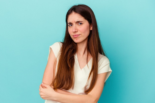 Jeune femme caucasienne isolée sur un mur bleu méfiante, incertaine, vous examinant.