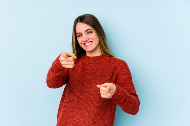 Jeune femme caucasienne isolée sur un mur bleu pointant vers l'avant avec les doigts.