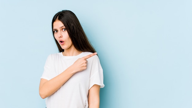 Jeune femme caucasienne isolée sur mur bleu souriant et pointant de côté, montrant quelque chose à l'espace vide.