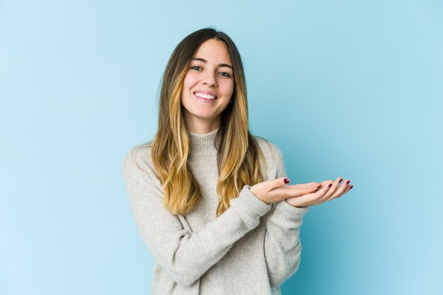 Jeune femme caucasienne isolée sur un mur bleu tenant un espace de copie sur une paume.