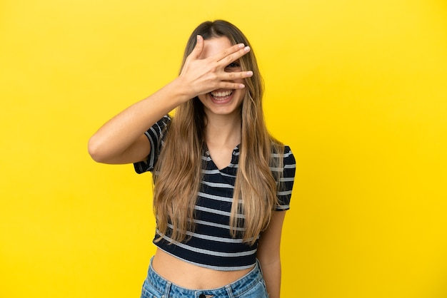 Jeune femme caucasienne isolée sur un mur jaune couvrant les yeux par les mains et souriant