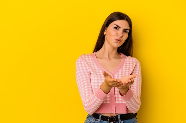 Jeune femme caucasienne isolée sur le mur jaune se pliant les lèvres et tenant les paumes pour envoyer le baiser de l'air.