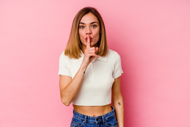 Jeune femme caucasienne isolée sur un mur rose en gardant un secret ou en demandant le silence.