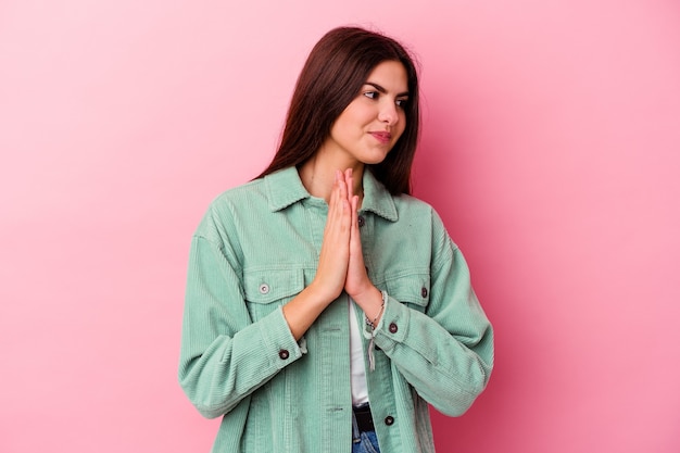 Jeune femme caucasienne isolée sur un mur rose priant, montrant la dévotion, personne religieuse à la recherche d'inspiration divine.